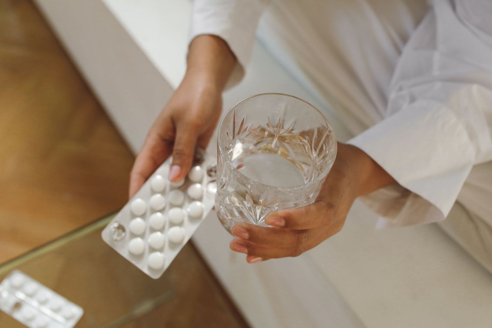 Person håller ett glas vatten och en blisterförpackning med vita tabletter